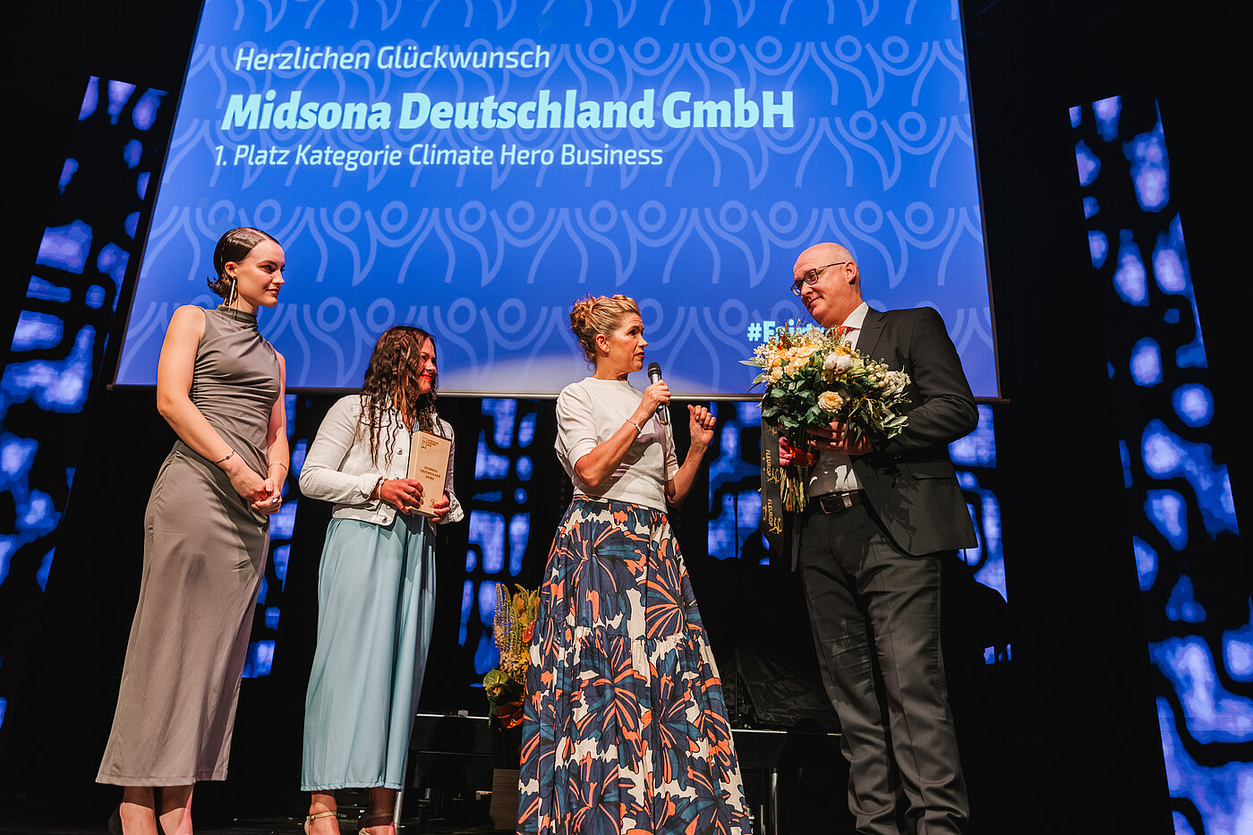 Auf der Bühne mit Anke Engelke und Laudatorin Louisa Schneider bei den Fairtrade Awards 2024: Gewinner des Fairtrade Awards in der Kategorie Climate Hero Business ist Midsona