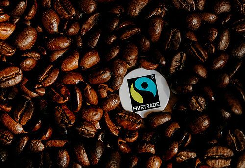 Ein Fairtrade-Siegel liegt inmitten von gerösteten Kaffeebohnen.