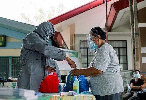 Ein Mensch in Corona-Schutzanzug verteilt Hygieneartikel. 