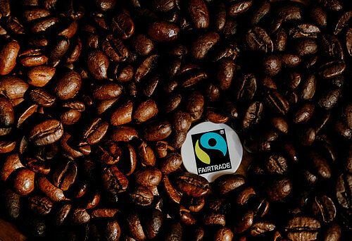 Ein Fairtrade-Siegel liegt inmitten gerösteter Kaffeebohnen.