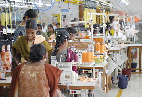 Mehrere Frauen arbeiten in einer Textilfabrik in Indien an der Nähmaschine. 