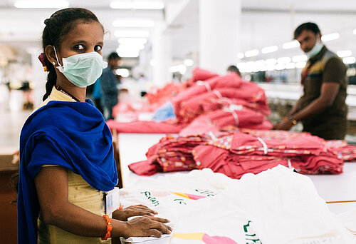 Eine indische Textilarbeiterin schaut in die Kamera - sie trägt einen Mundschutz.