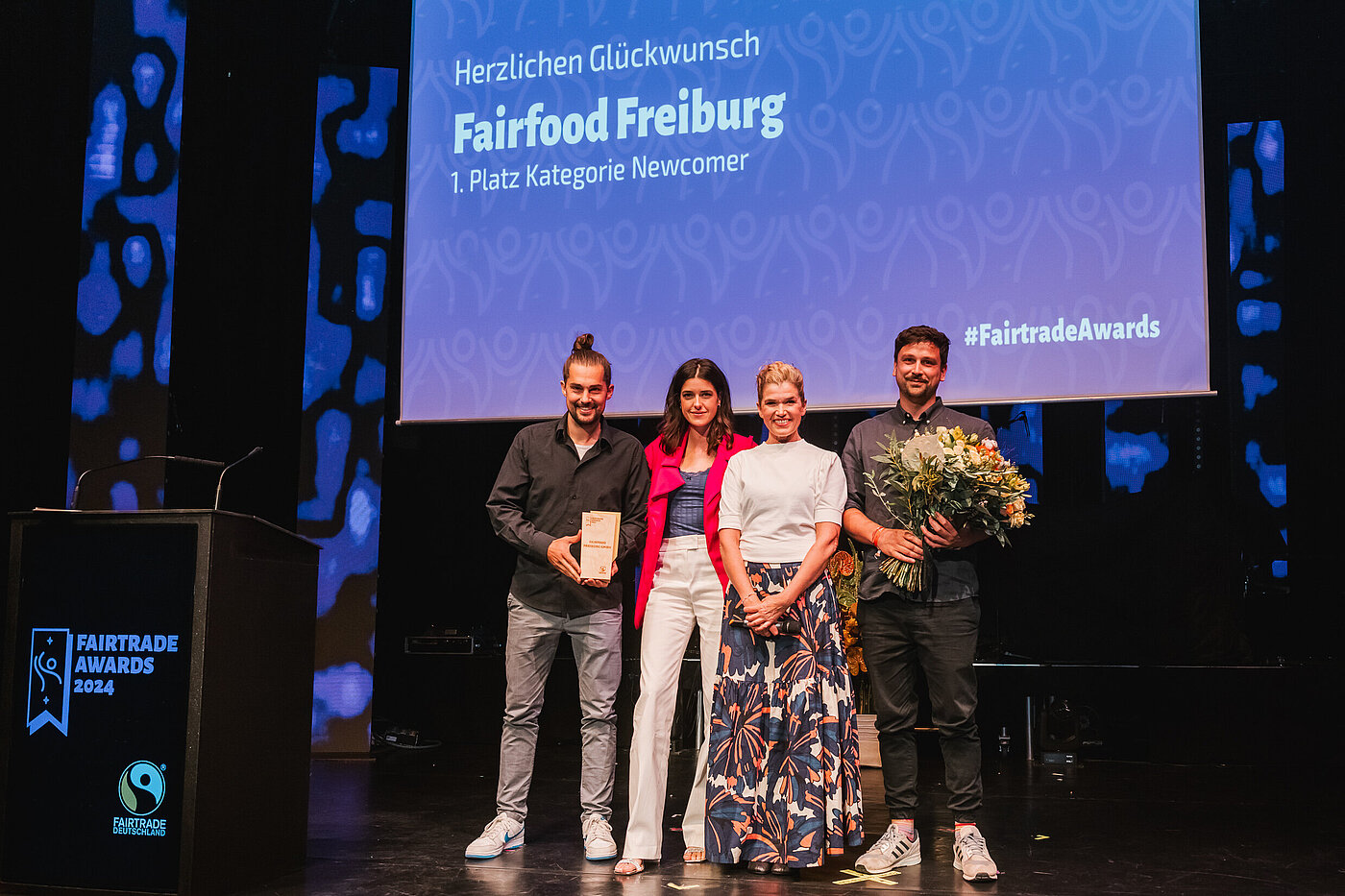 Auf der Bühne mit Anke Engelke und Laudatorin Marie Nasemann bei den Fairtrade Awards 2024: Gewinner des Fairtrade Awards in der Kategorie Newcomer ist fairfood Freiburg