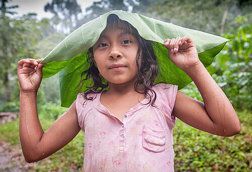 A young girl protects herself from the rain with a malanga leaf at a CORCASAN coffee farm in San Juan de Rio Coco.